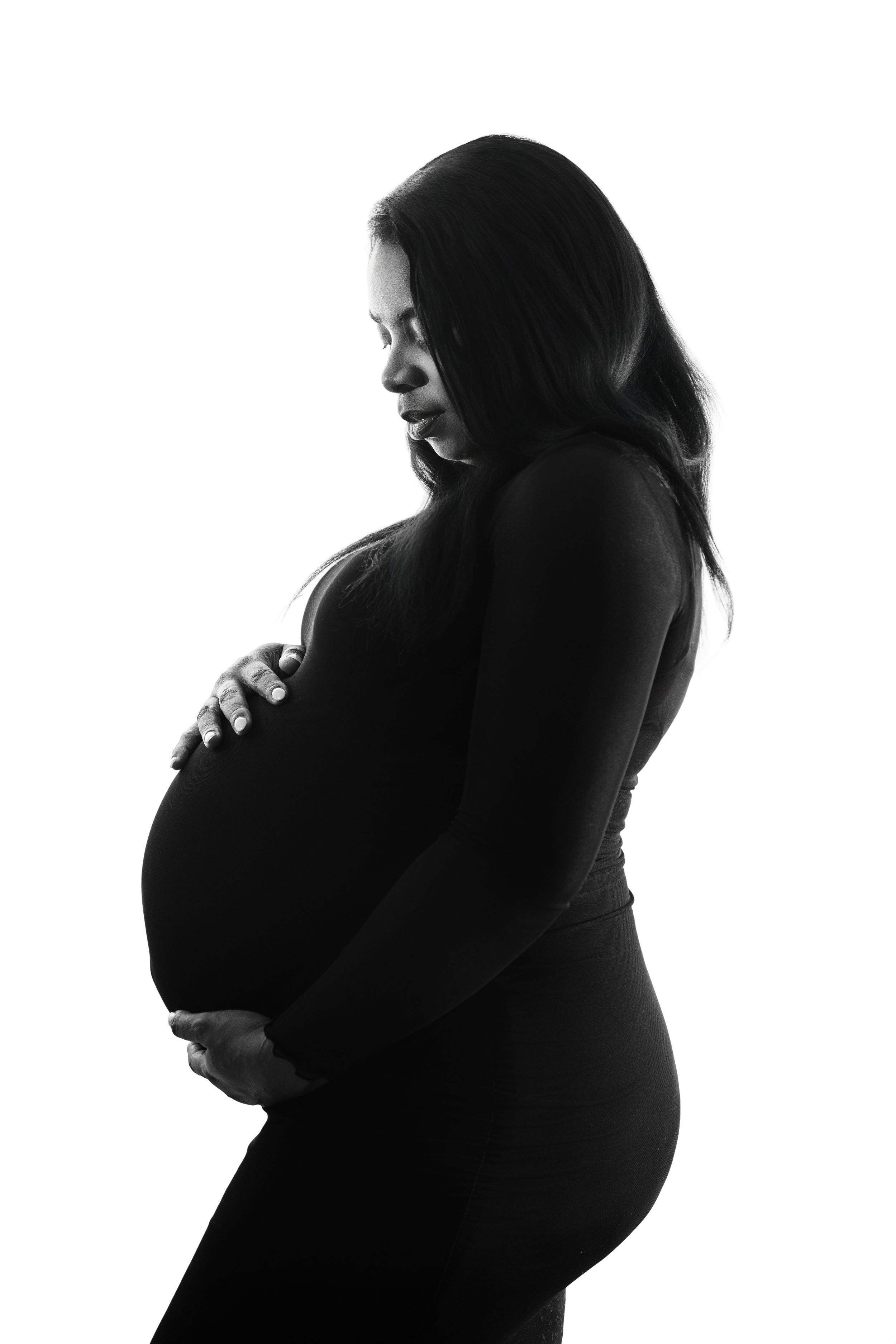 Black and white silhouette portrait of an expectant mother in profile tenderly holding her pregnant belly.