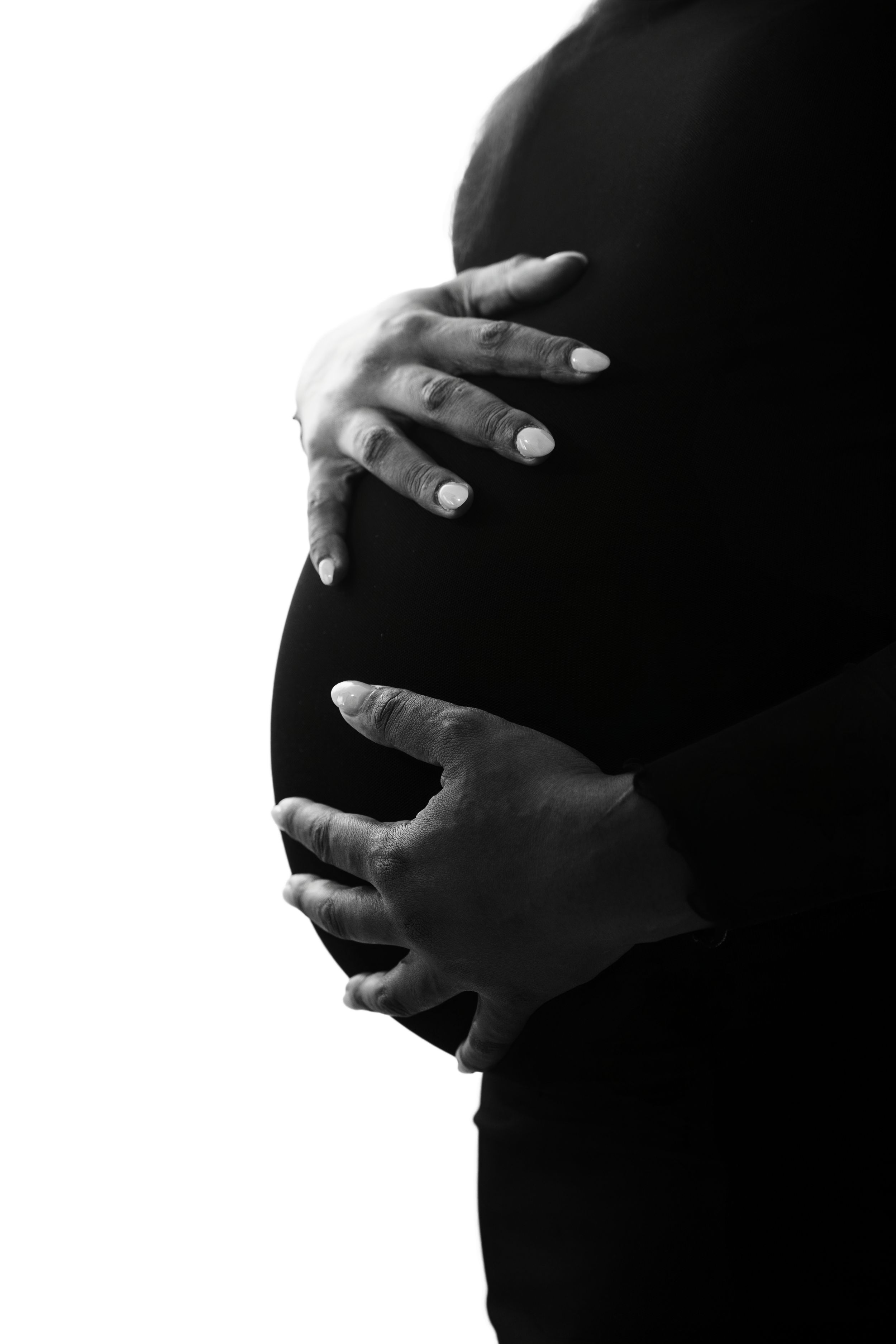 Silhouette of hands cradling a pregnant belly against a dark background in black and white.