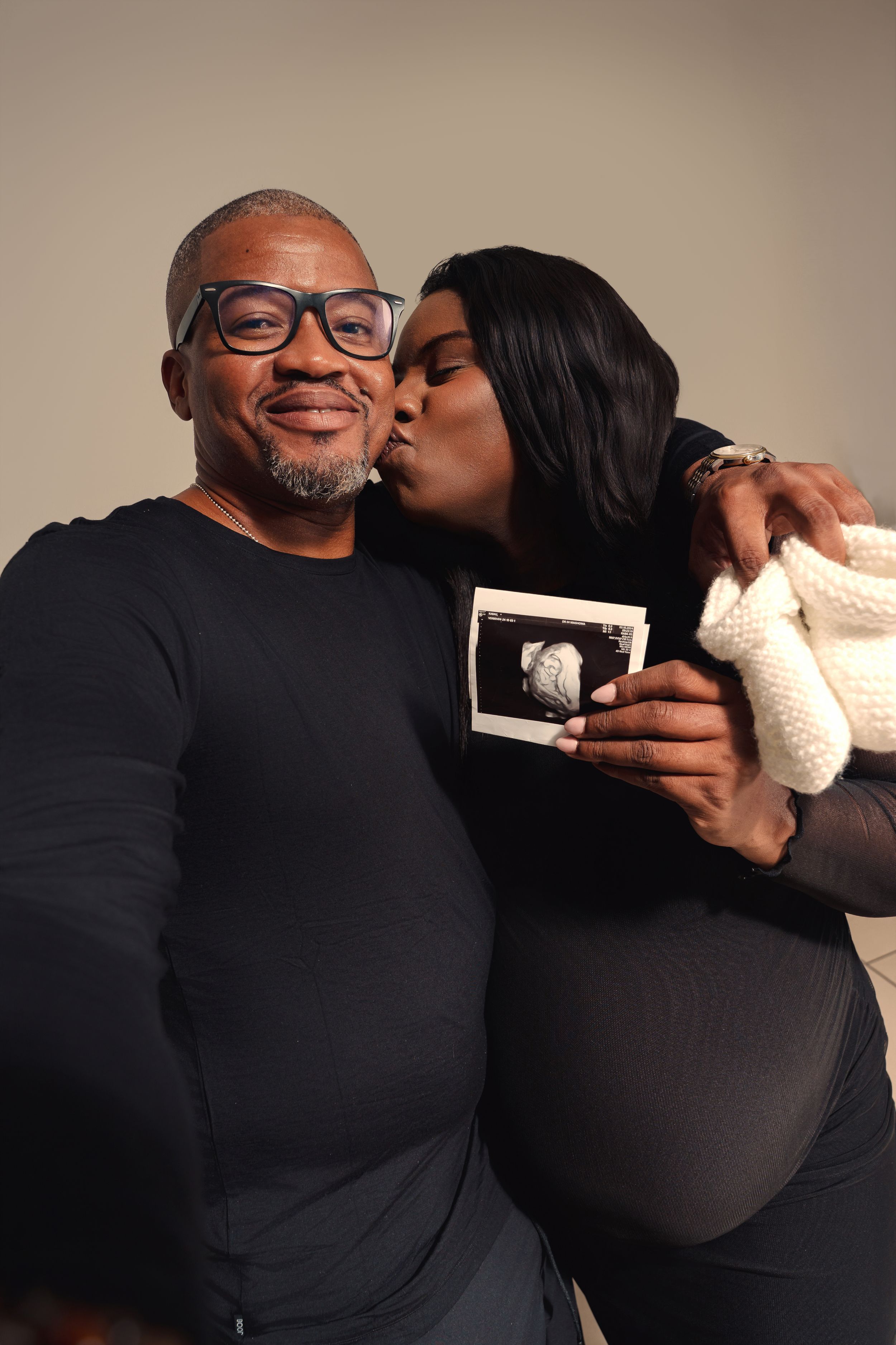 Expectant couple shares intimate moments while holding ultrasound photos in a professional studio setting.