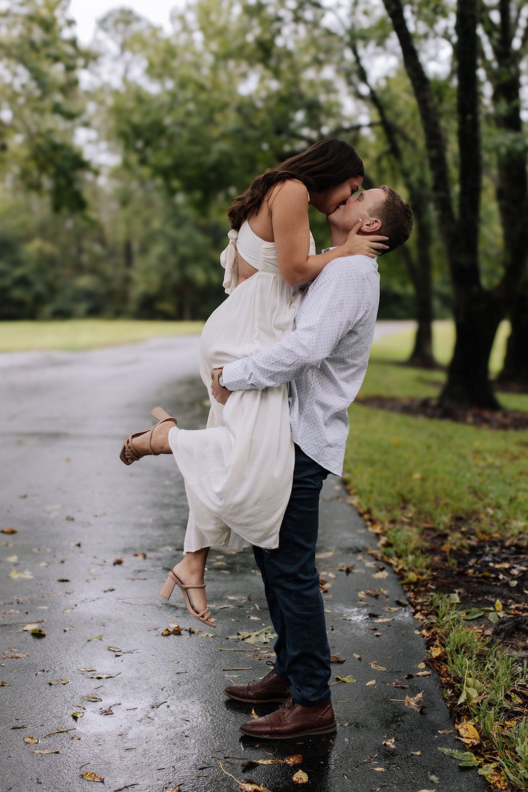 A romantic couple embraces and kisses on a wooden dock by the water on an overcast day.