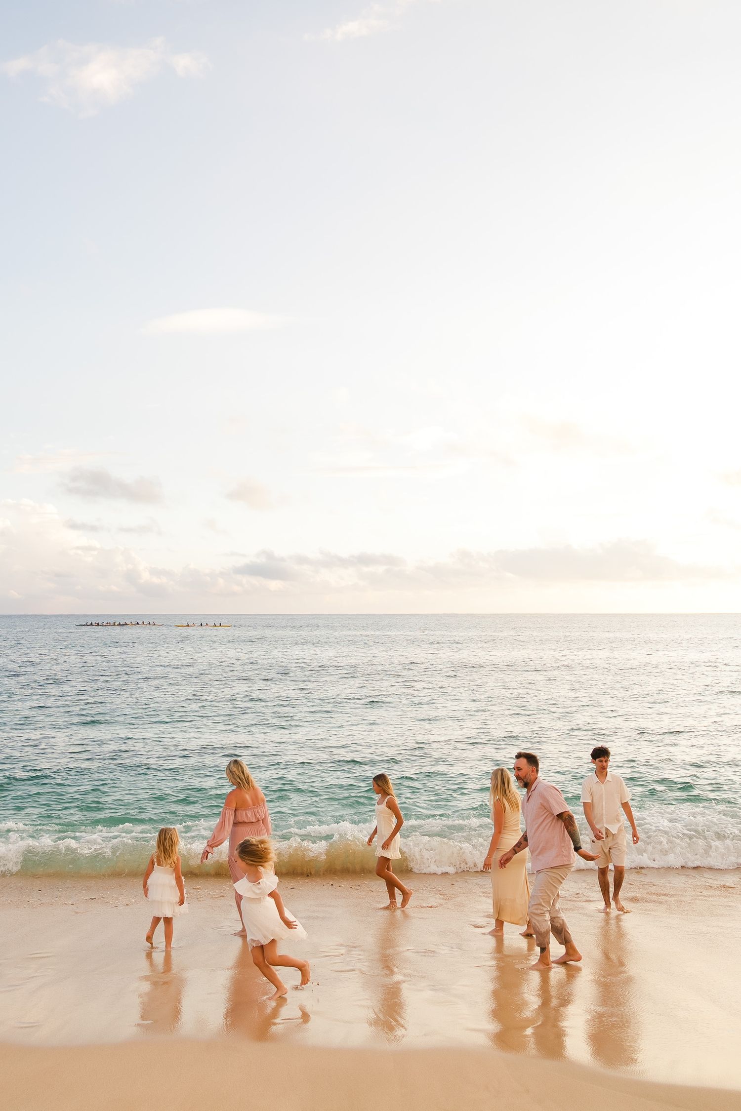 A group of people in white and beige clothing running and playing together on a sandy beach at sunset.　Oahu Family Photographer | Aya S Tomi