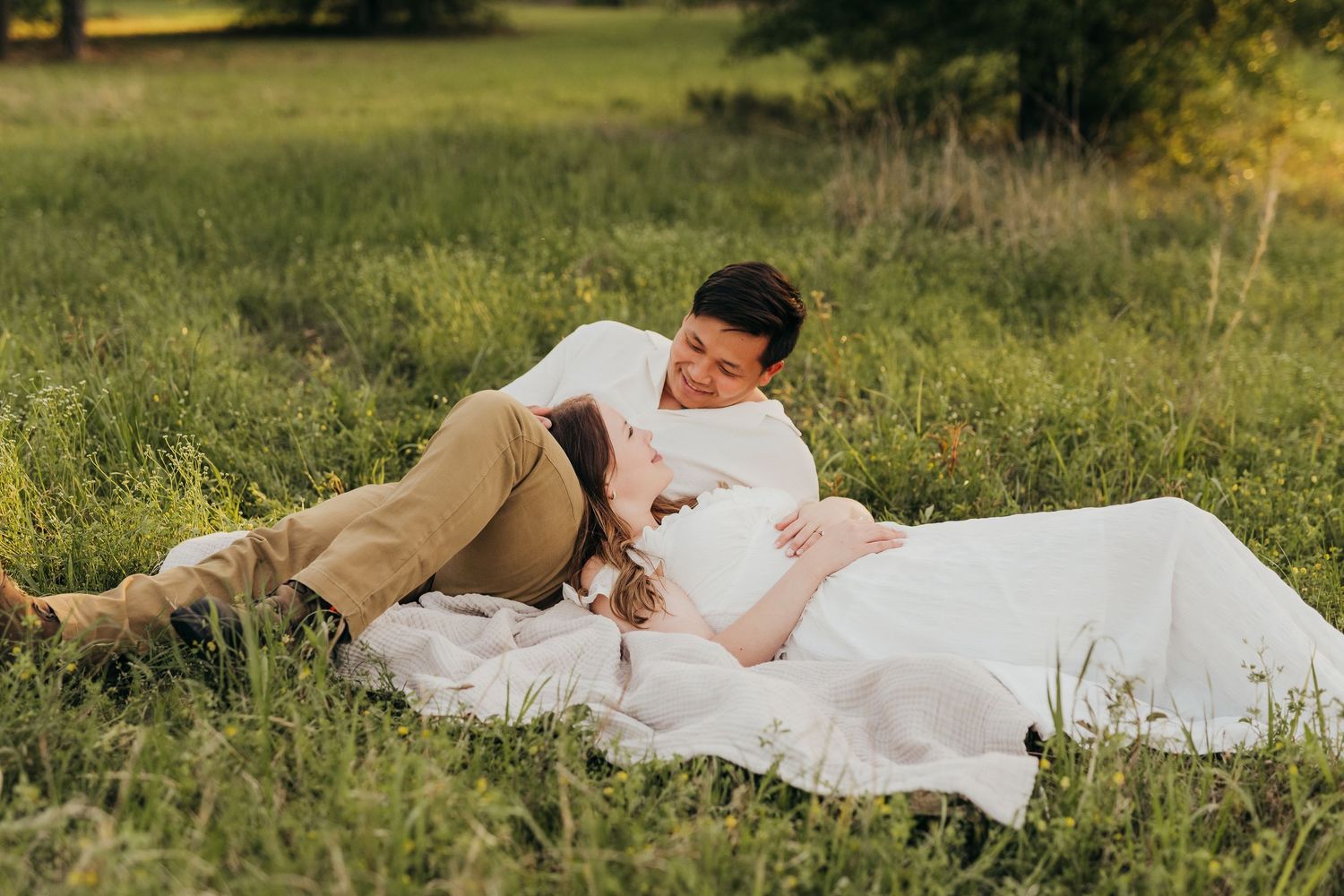 A couple in wedding attire lies together on lush green grass during a romantic outdoor photo session at sunset in Tyler, Tx.