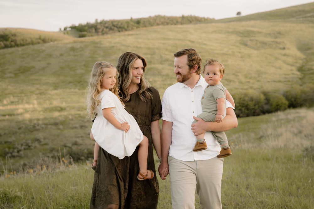 Family enjoying a peaceful moment together on rolling grassy hills during sunset.