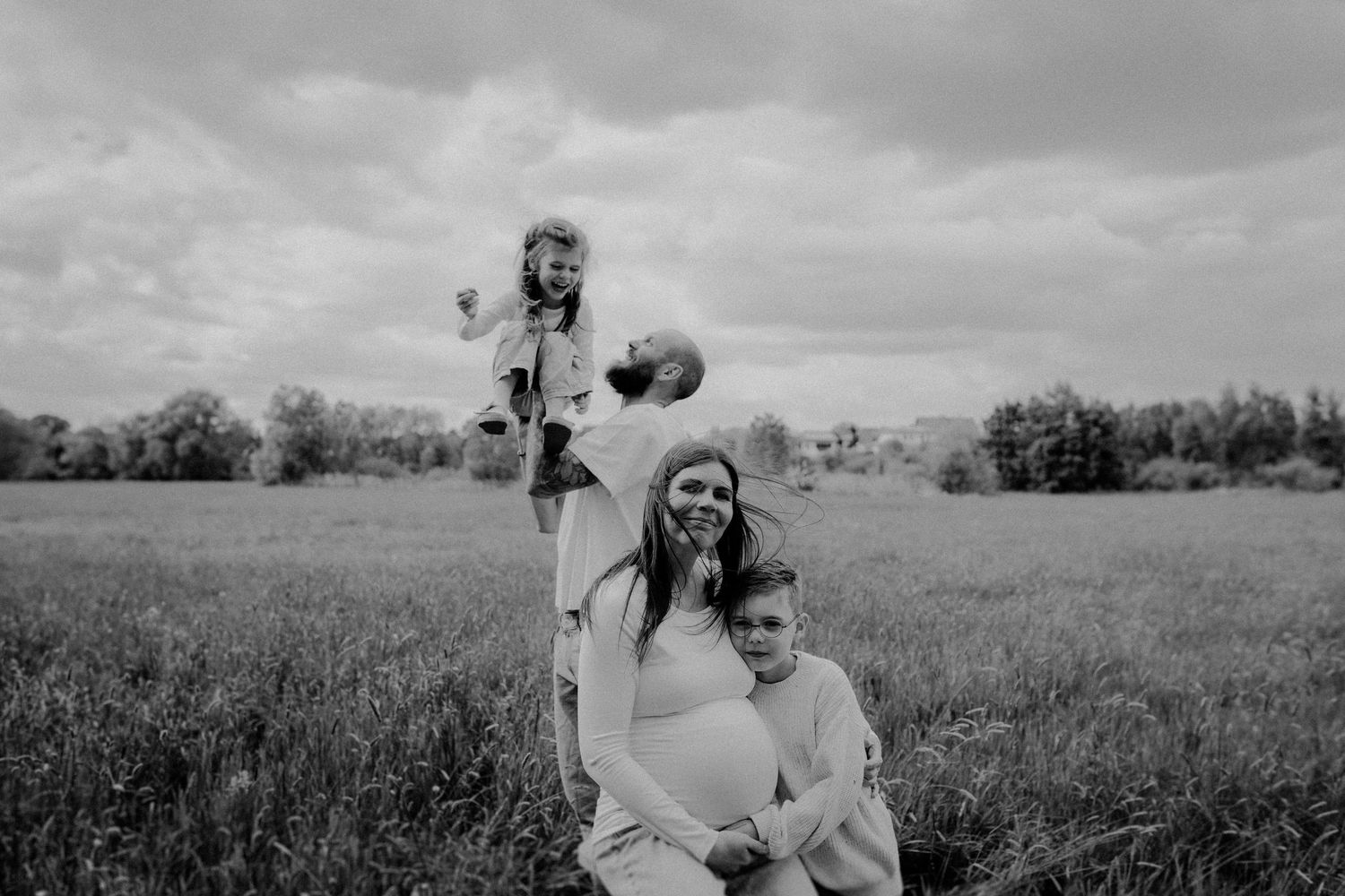 Der Papa wirfst die Tochter hoch in die Luft, sie lacht herzhaft. Davor sitzt die schwangere Mama und kuschelt mit ihrem Sohn. Der Wind weht