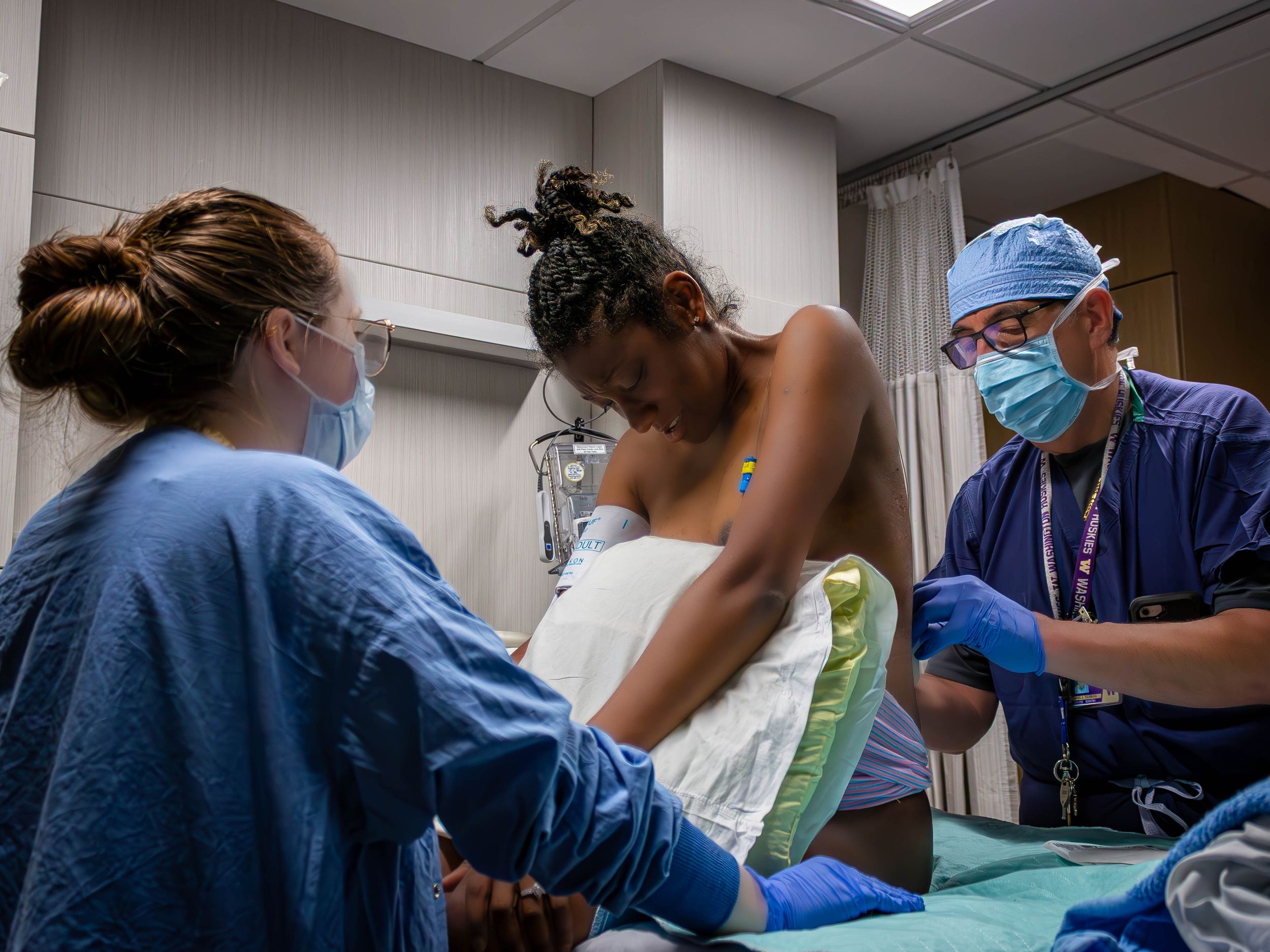 Medical professionals in blue scrubs and masks attend to a patient on an examination bed during a medical procedure.