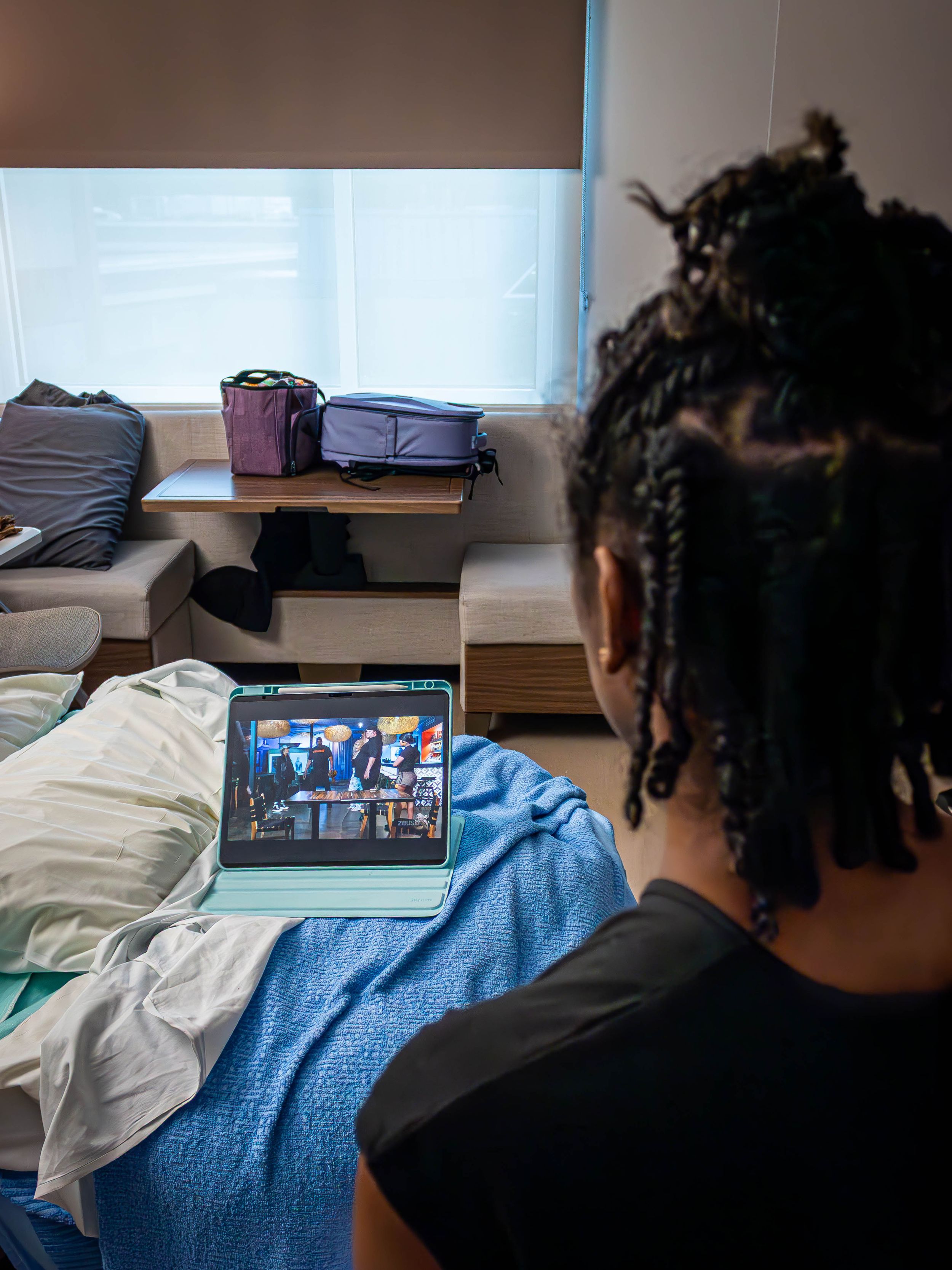 Someone watching a tv show on a laptop while sitting on a bed with blue bedding in a hospital room.
