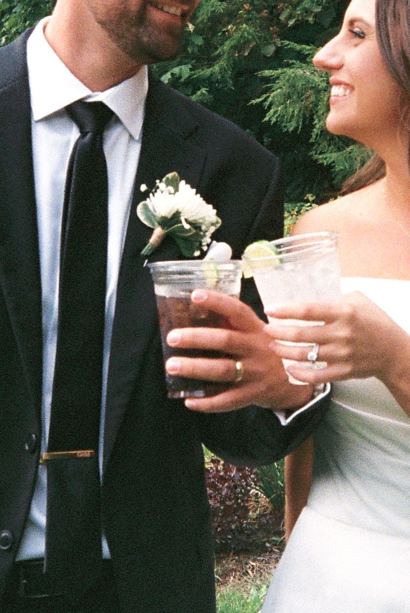 Close-up of couple holding cocktail glasses during outdoor wedding reception.