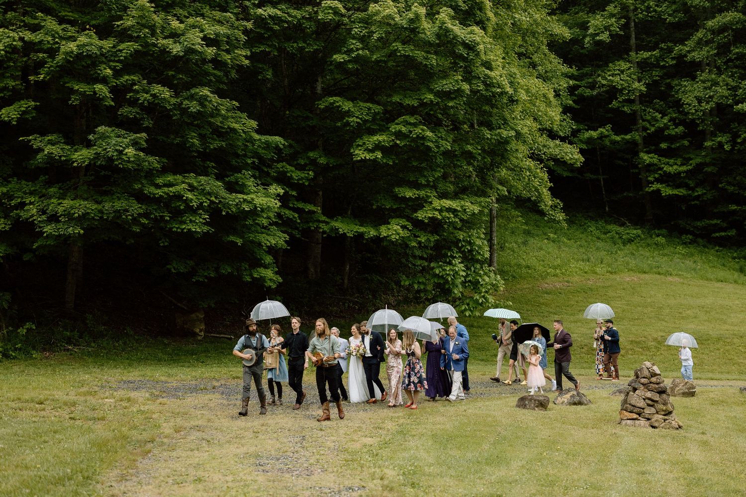 A group of people in formal attire stand in a line together on a grassy hill during a daytime outdoor event.