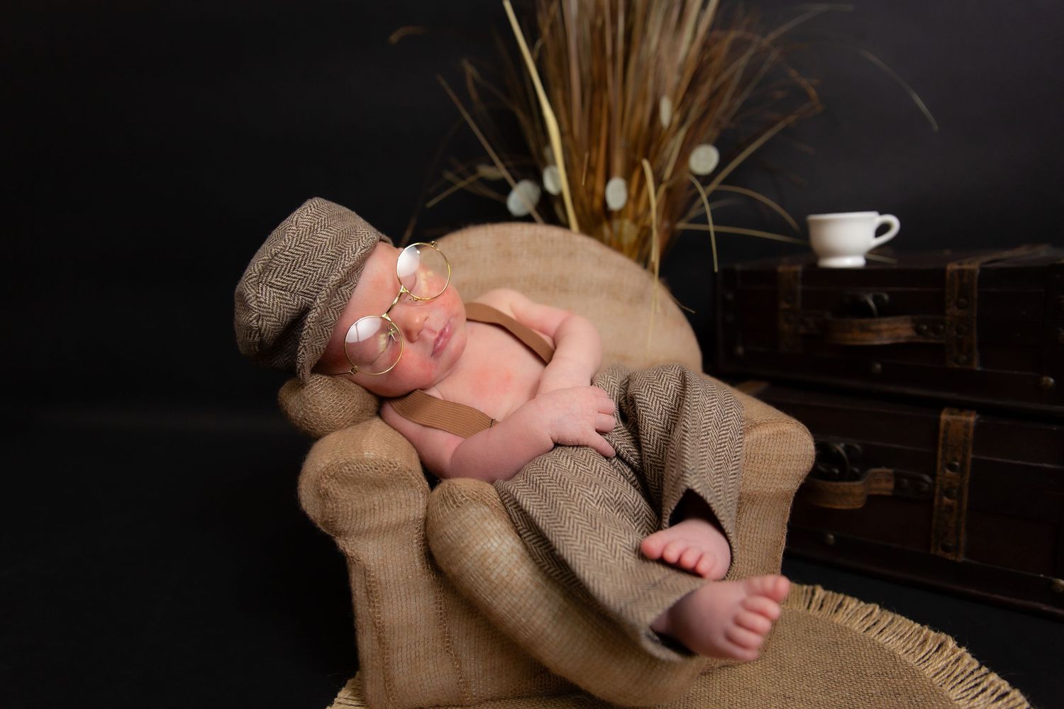 A peaceful newborn baby sleeps on a brown armchair wearing a knit cap in a dark studio setting.