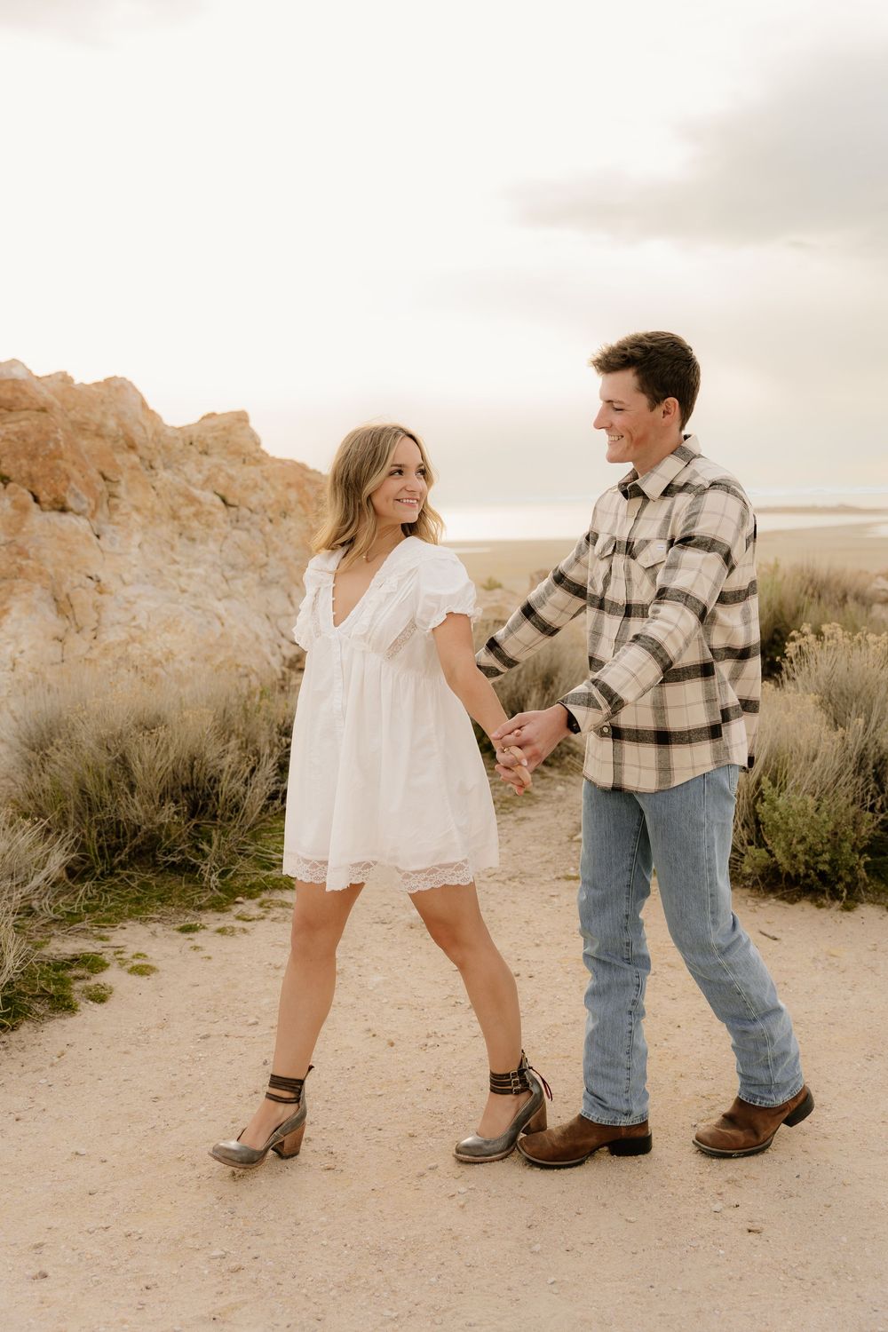 Couple dancing on a desert trail wearing casual western attire at sunset.