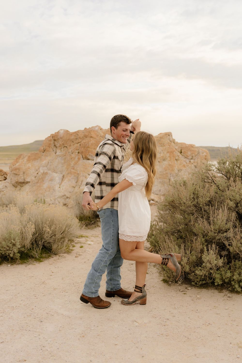 Romantic couple in coordinated outfits share intimate moment on desert trail near rock formations.