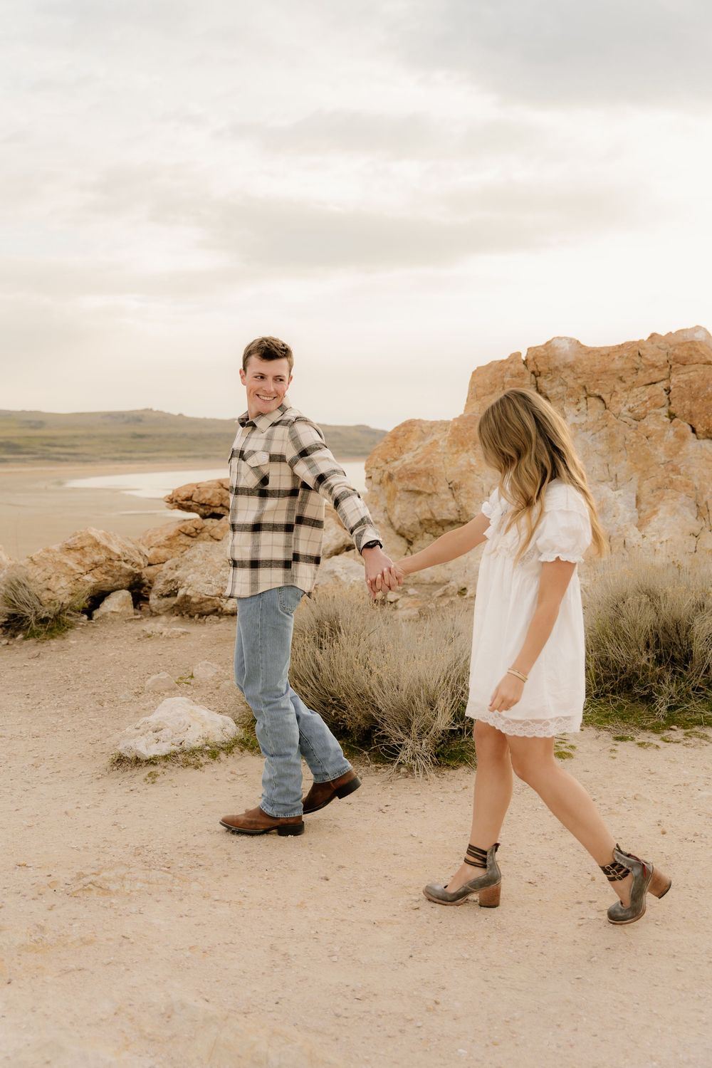 Couple walks hand in hand along desert path near rock formations.