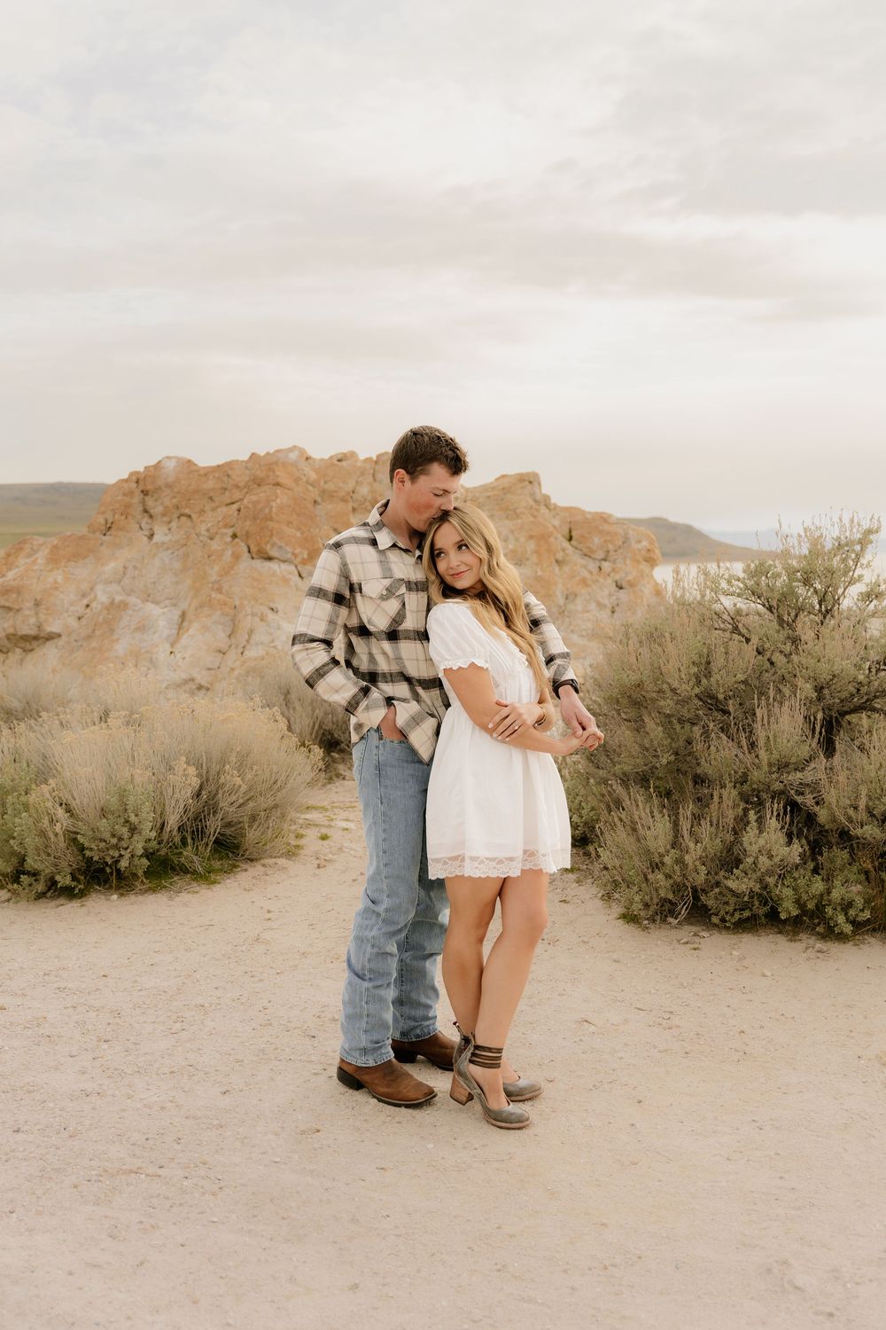 A sweet moment captured in the desert landscape as a couple bends down to interact with their dog on sandy ground.