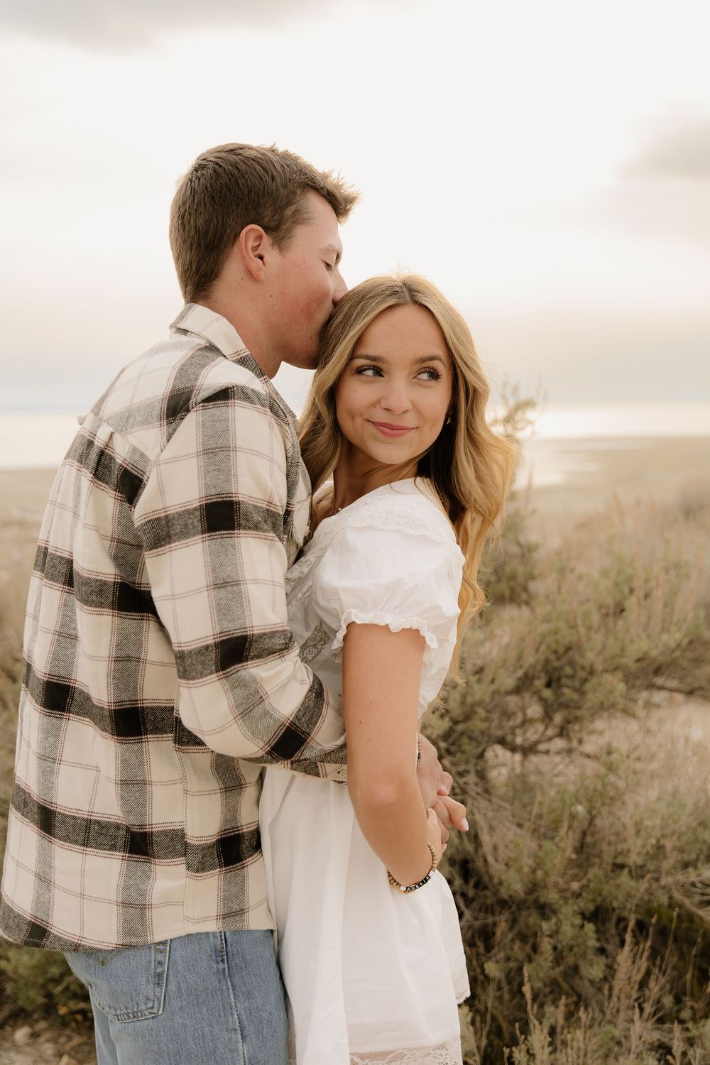 A tender desert photoshoot moment with a couple in casual attire against a desert landscape.