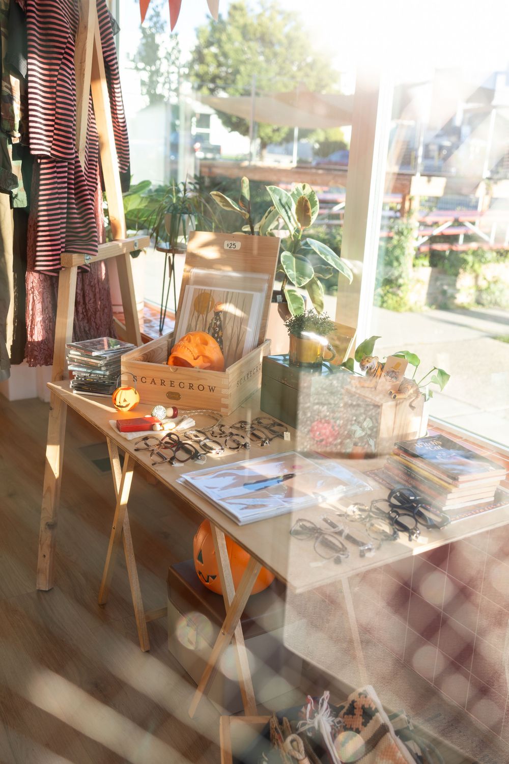 Sunlit retail display with wooden crates, clothing racks and vintage decor in a boutique shop window.