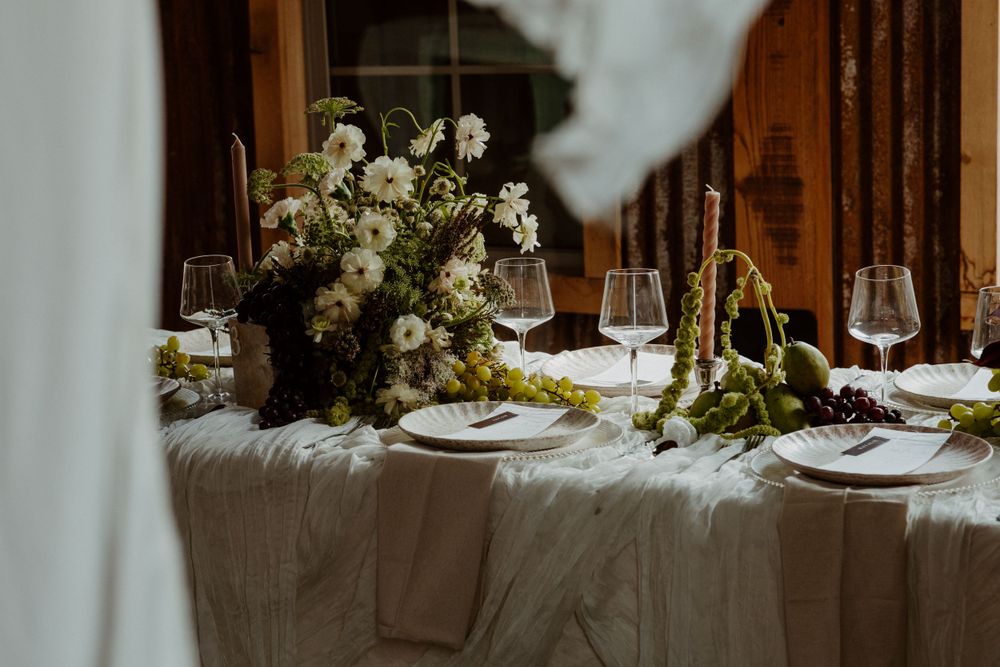 An elegant wedding table setting with white linens, wine glasses, and floral centerpieces captured behind a curtain.
