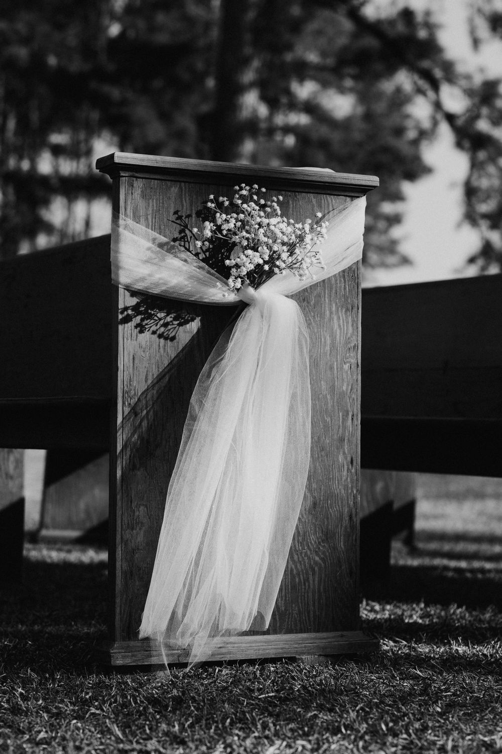 A detailed black and white photo the wedding aisle including breath flowers draped on wooden church pew.