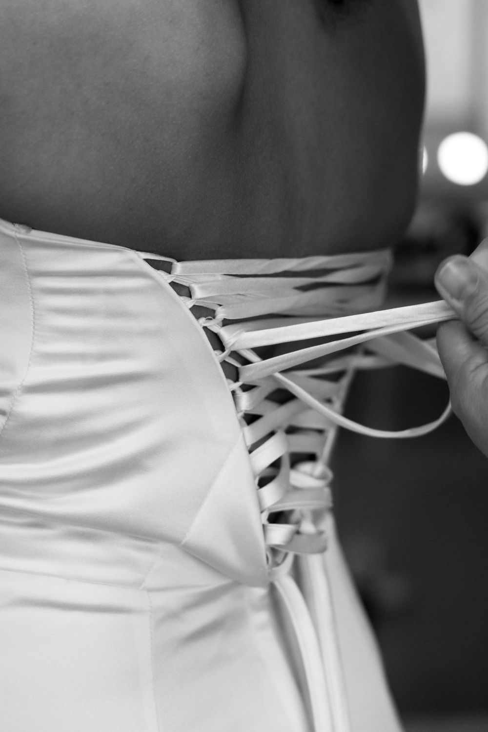 Detail shot of a white wedding dress being laced up in the back in black and white.