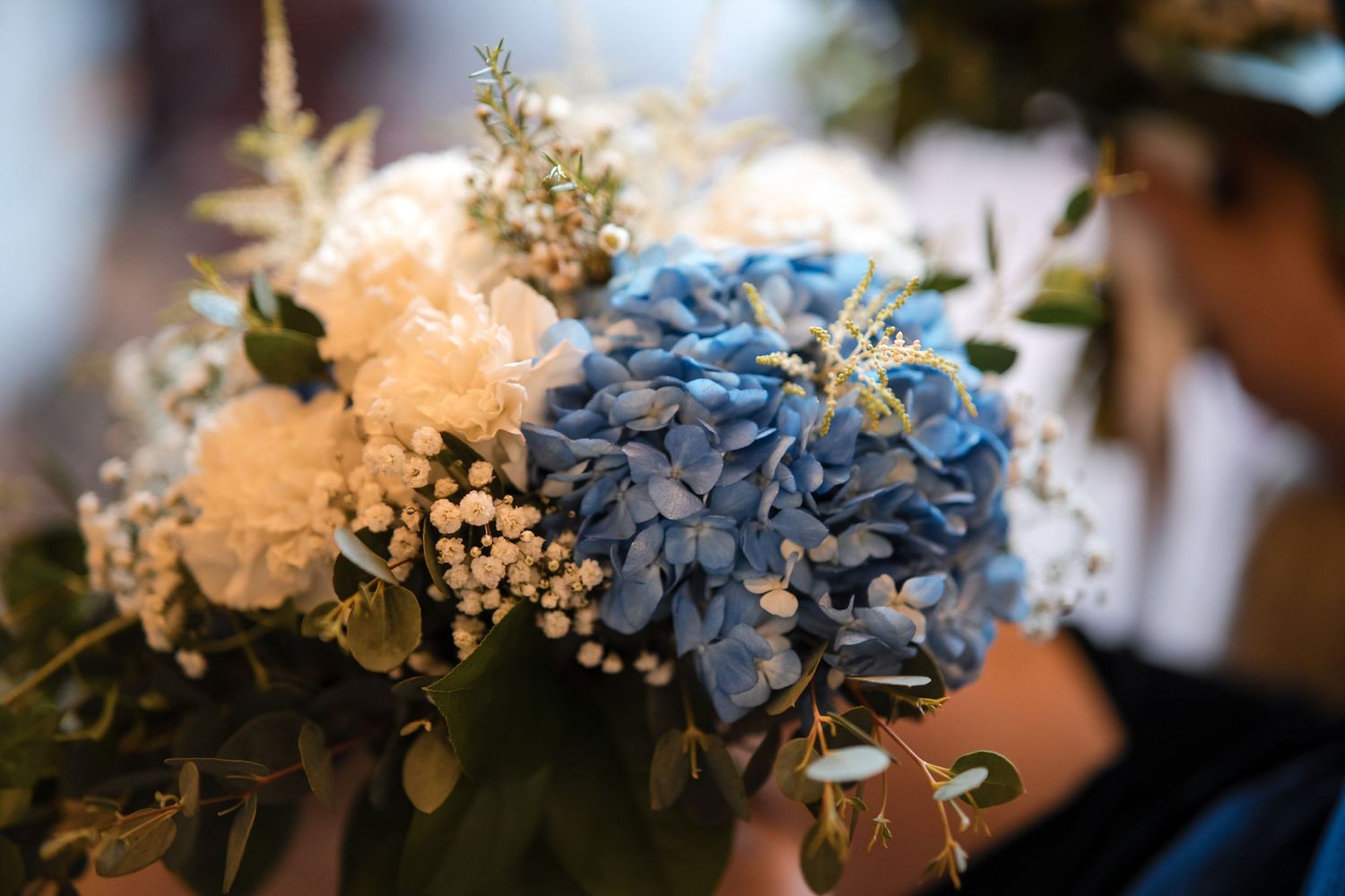 Elegant wedding bouquet with blue hydrangeas and white blooms against a soft background.