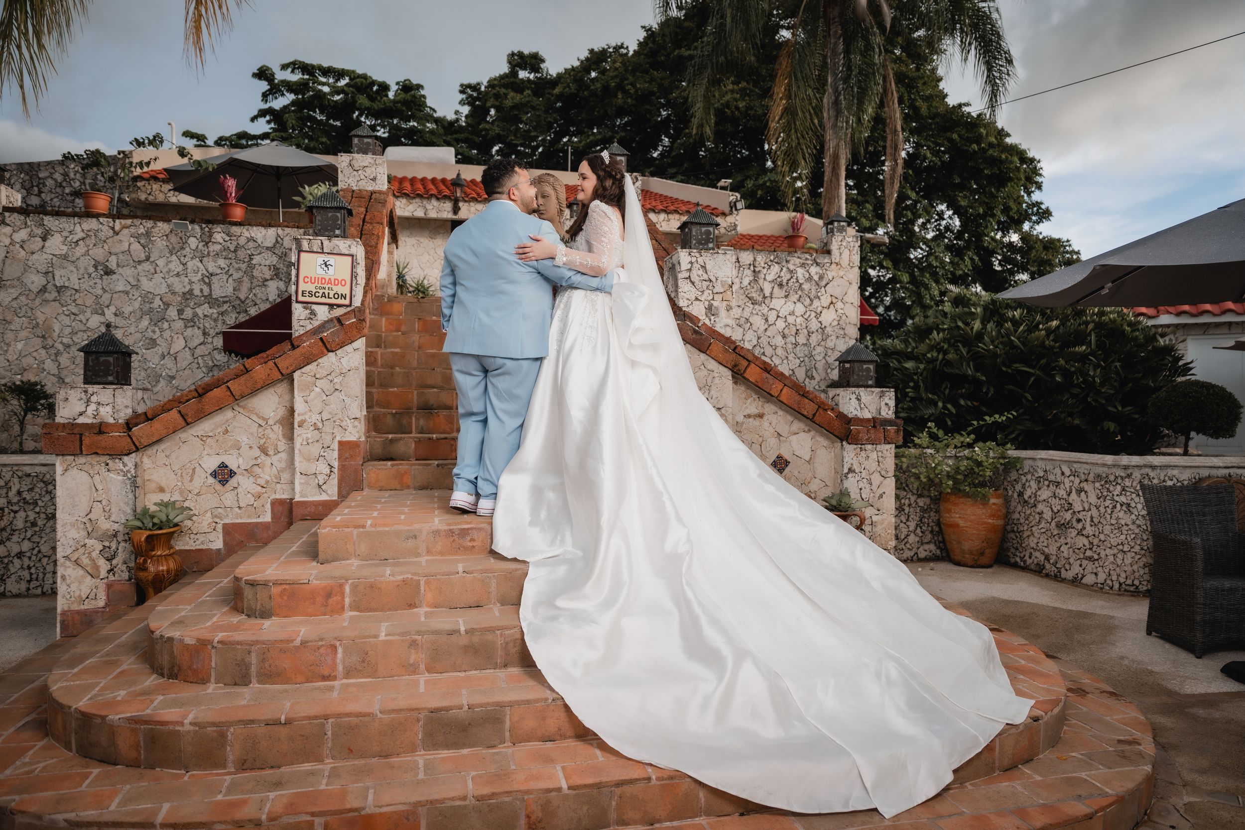 Wedding couple ascending stone steps with dramatic trailing white dress.