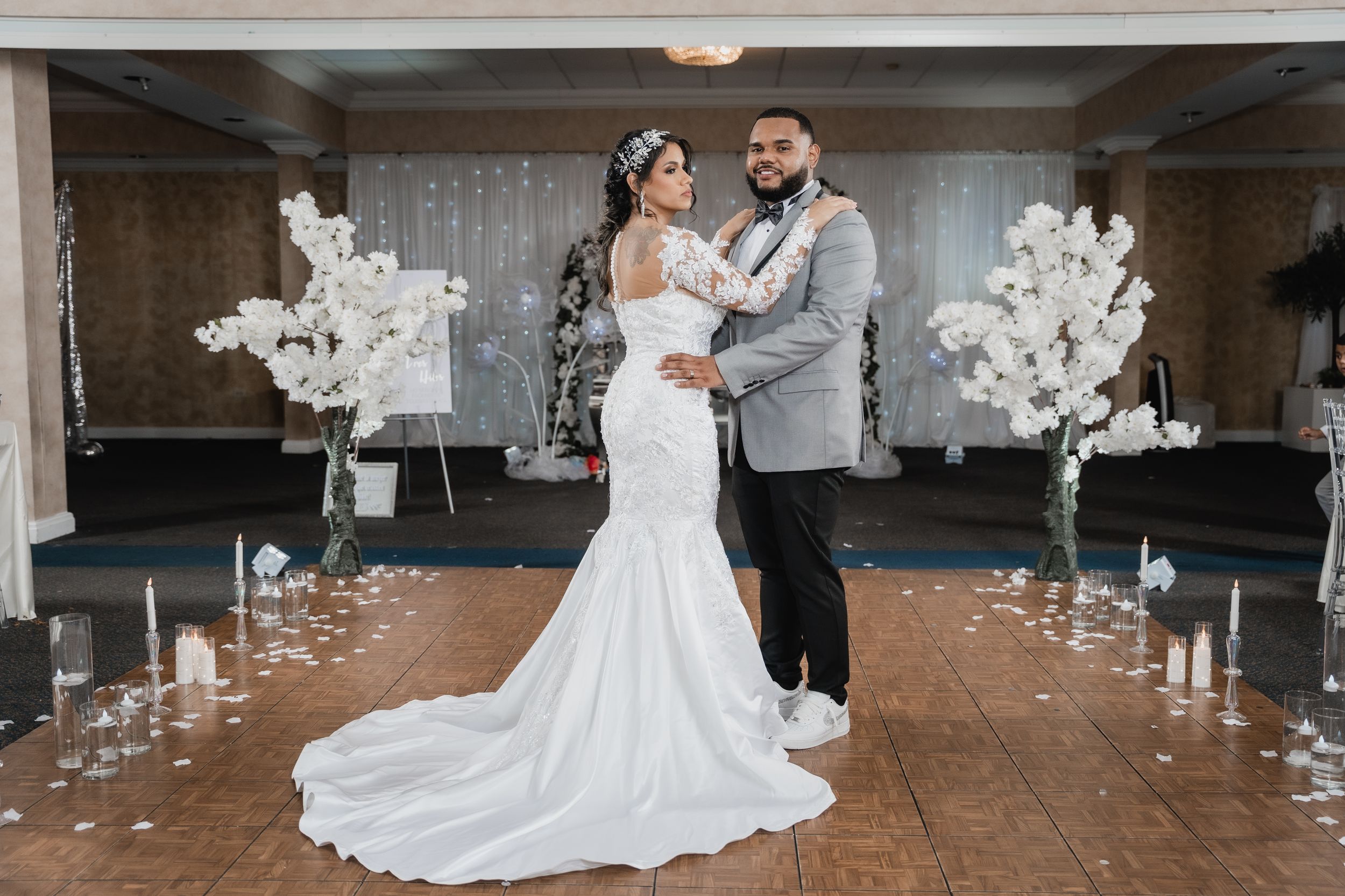 Wedding couple dancing in elegant venue with white floral arrangements and string lights.