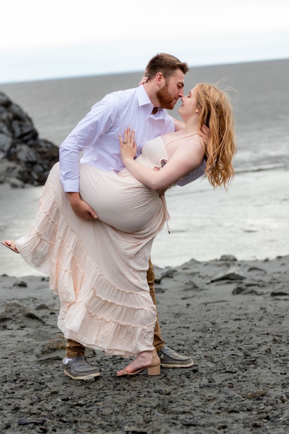 A romantic couple embraces on a black sand beach with dramatic dip pose.
