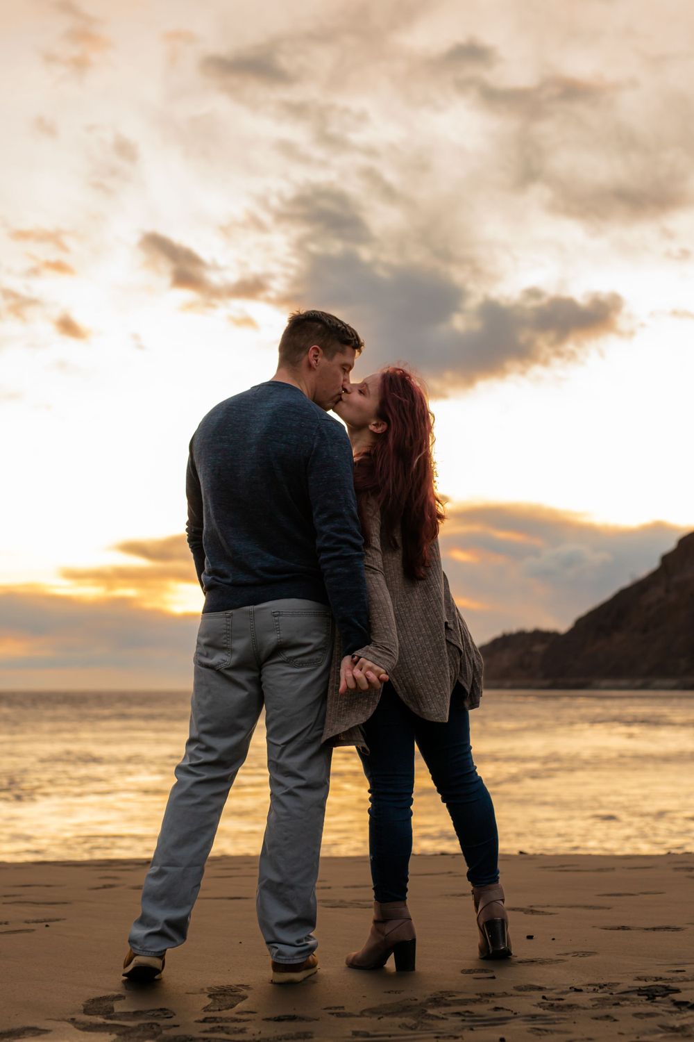 A romantic couple shares an intimate moment on a beach at golden hour.