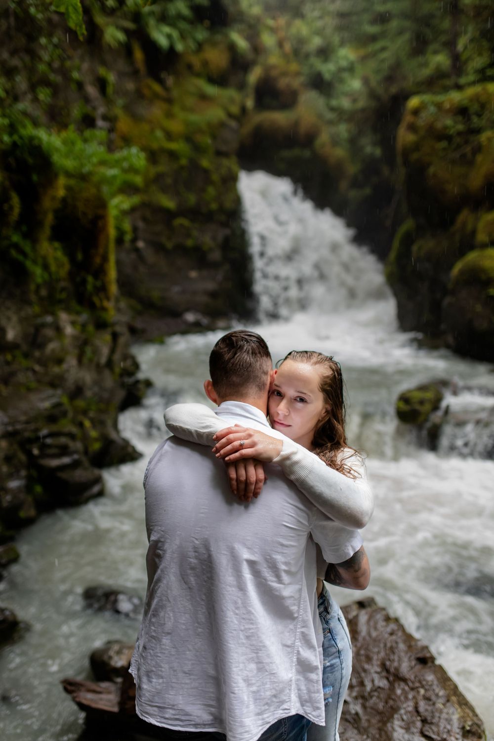 A couple shares tender embrace in front of dramatic waterfall landscape.