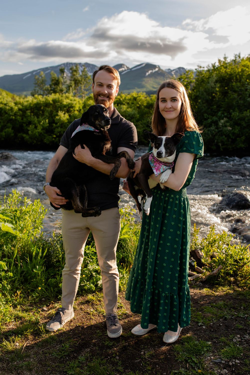 Couple poses with their two dogs by mountain stream on sunny summer day.