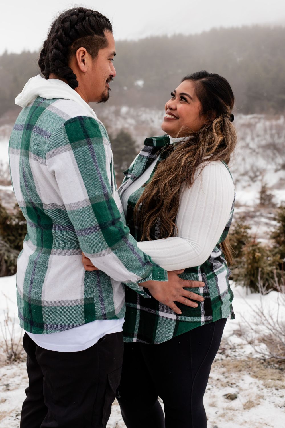 Couple in matching plaid flannel shirts share intimate moment in snowy winter landscape.