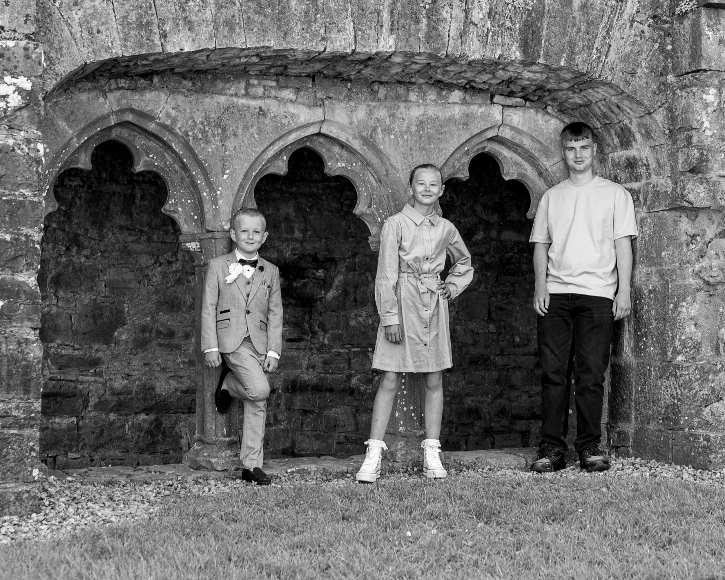Three figures stand in stone archways of an old building in a black and white photo.