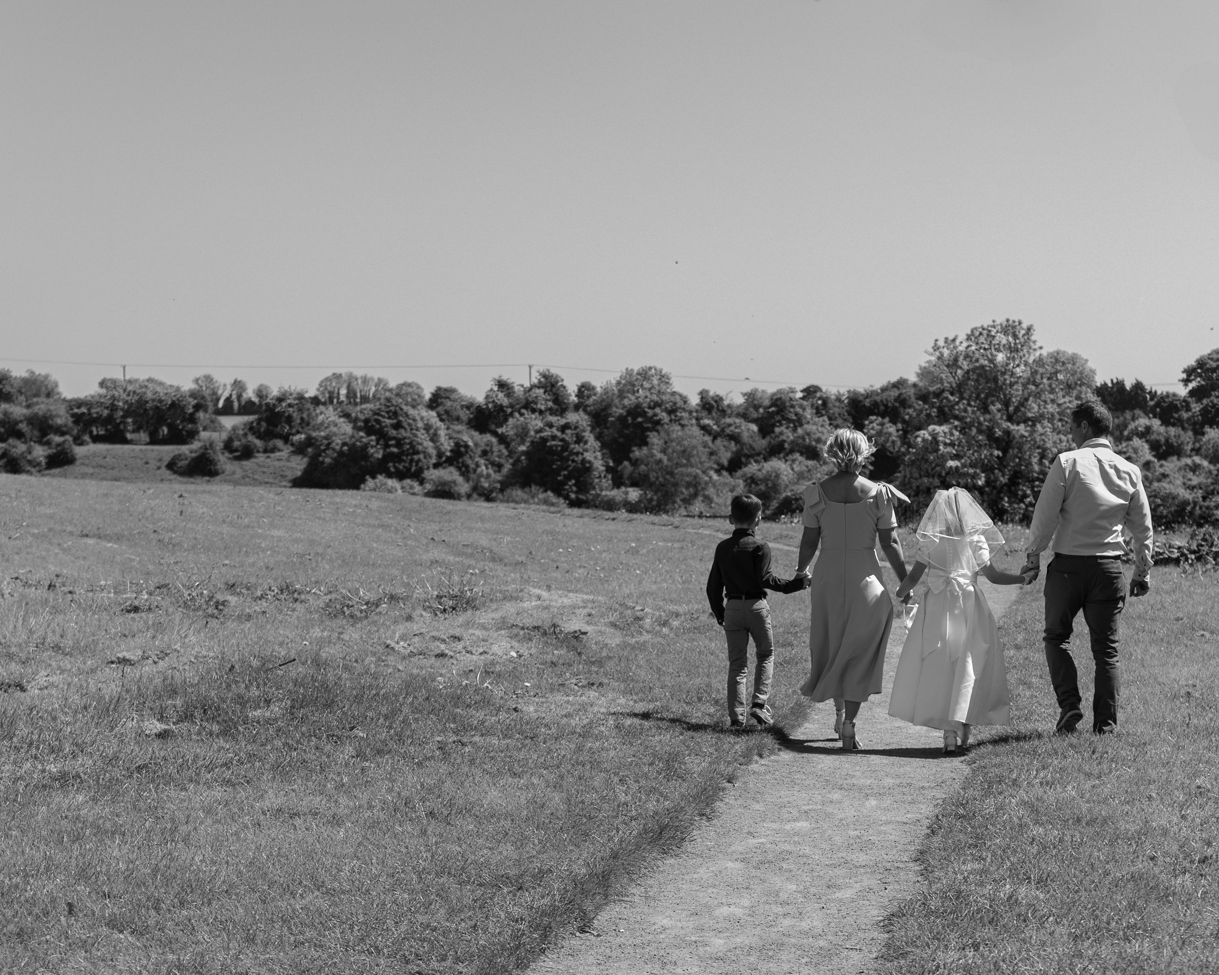 Wedding party walking across an open field on a sunny day.