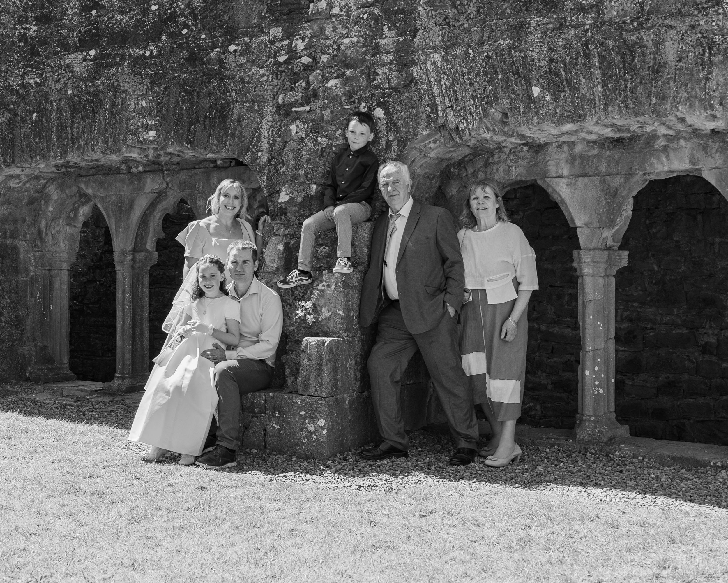 A group poses against stone archways in a black and white photograph at a historic site.