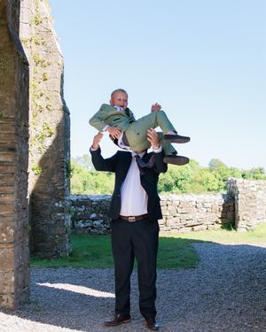 A person in formal attire lifts someone up in front of stone ruins.