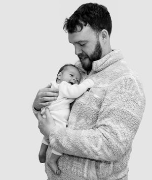 A tender moment captured in black and white as a parent in a fuzzy sweater cradles a sleeping newborn.