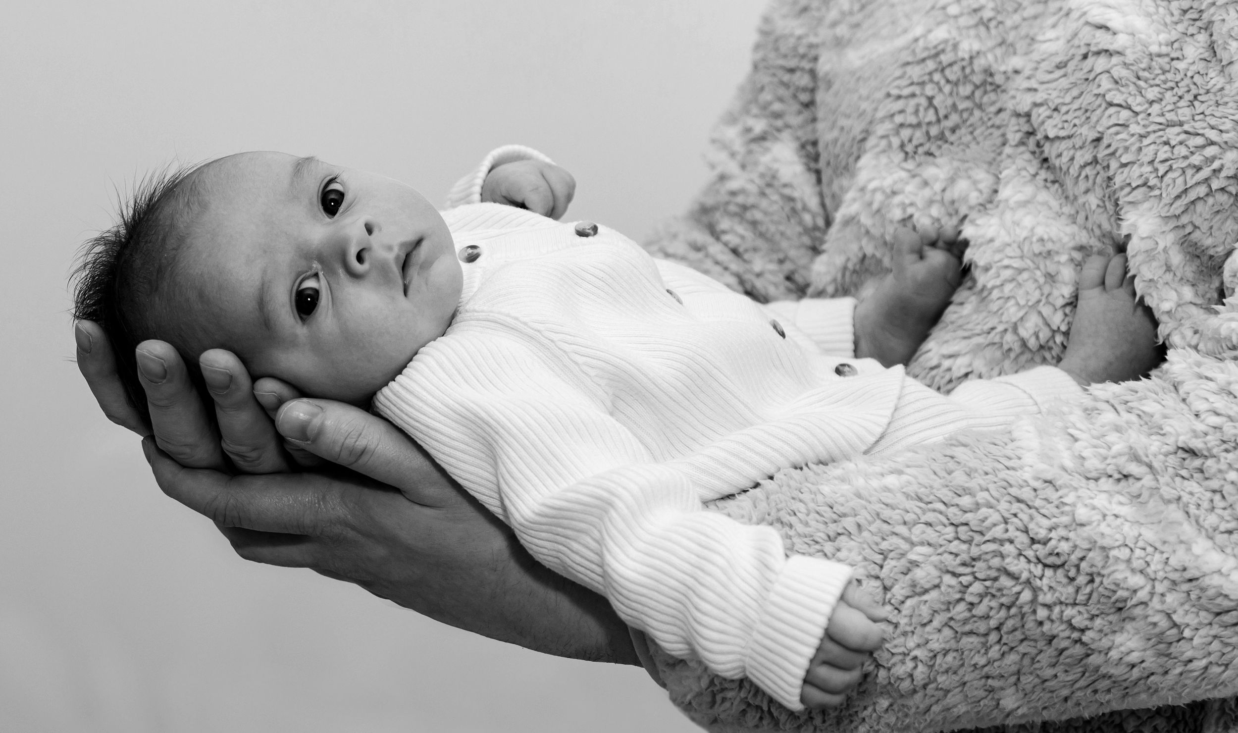 Black and white portrait of a newborn baby lying on soft textured blanket.