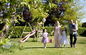 Happy family with children playing in a lush green garden with a wooden play area on a sunny day.