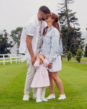 Family portraits showing sweet interactions on a grassy field with white fence and pine trees.