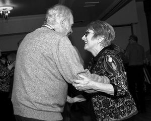 Black and white photo of elderly people dancing or embracing at a social gathering.