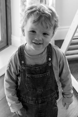 Adorable toddler in denim overalls and white shirt smiling at the camera in a series of candid indoor shots.