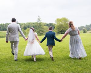 Four people holding hands while skipping through a green field during a wedding celebration.