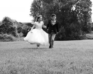 A vintage black and white photo of newlyweds running playfully across a grassy field.