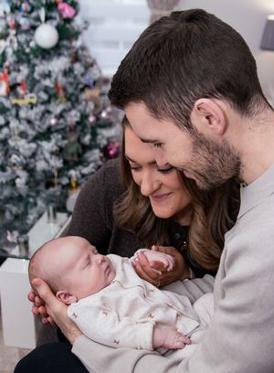 Holiday photos with a Christmas tree showing tender family moments with a baby in white clothing.