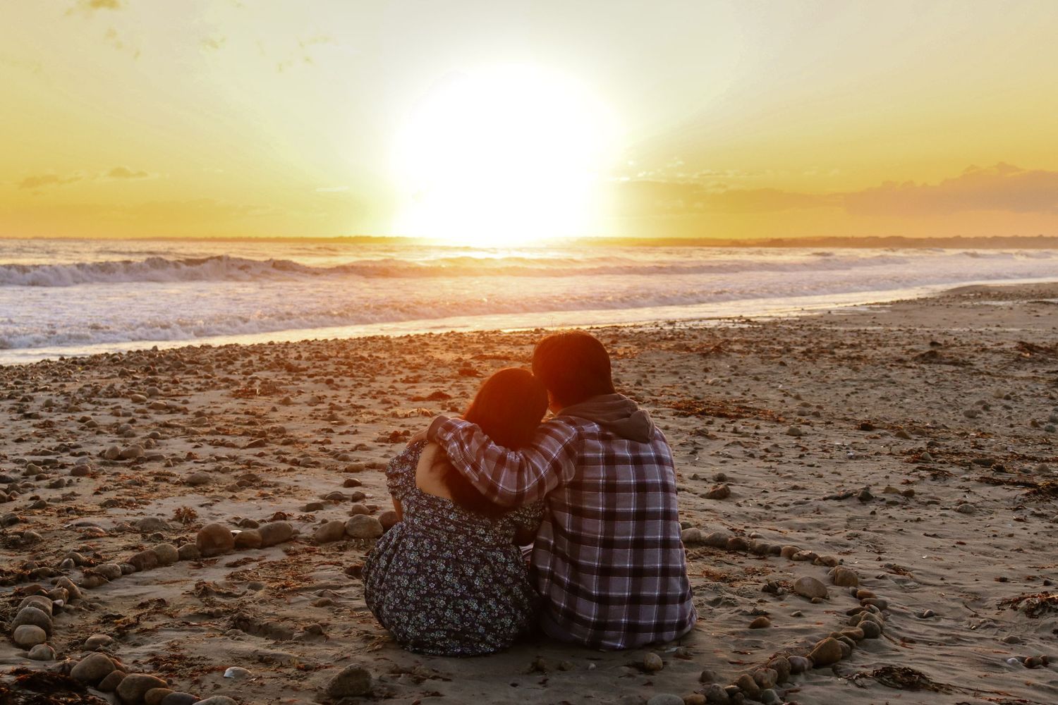 Couple watching sunset together on sandy beach.