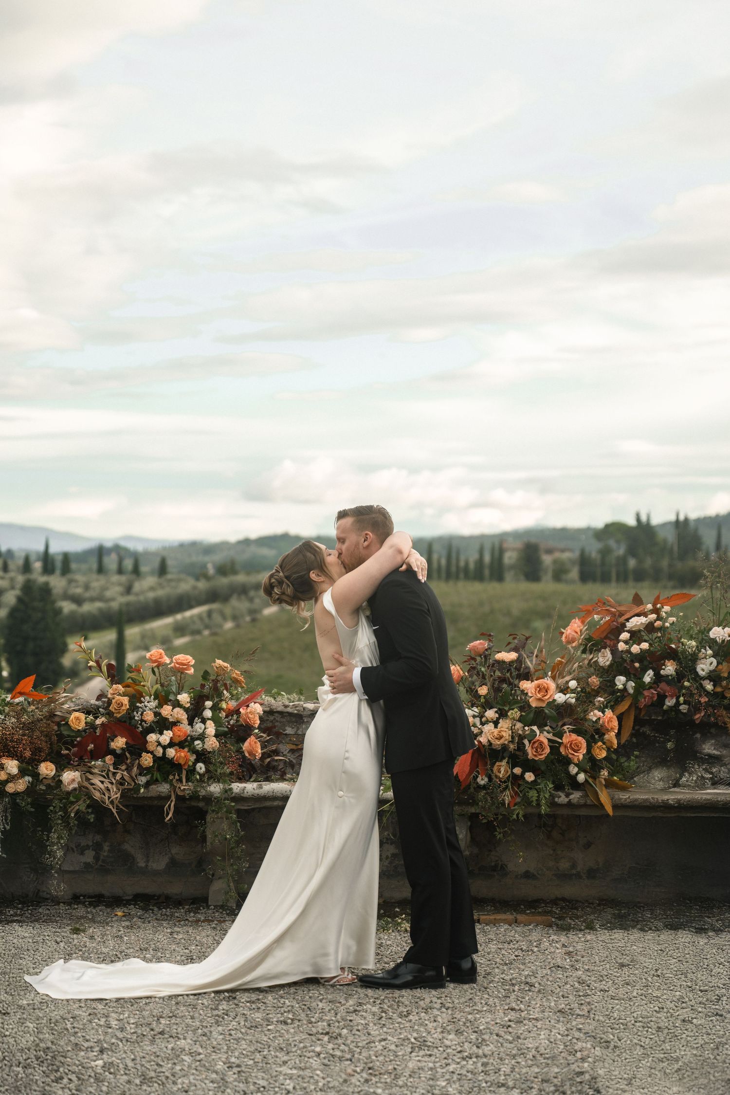 Couple shares romantic moment against scenic Tuscan landscape with orange floral decorations.