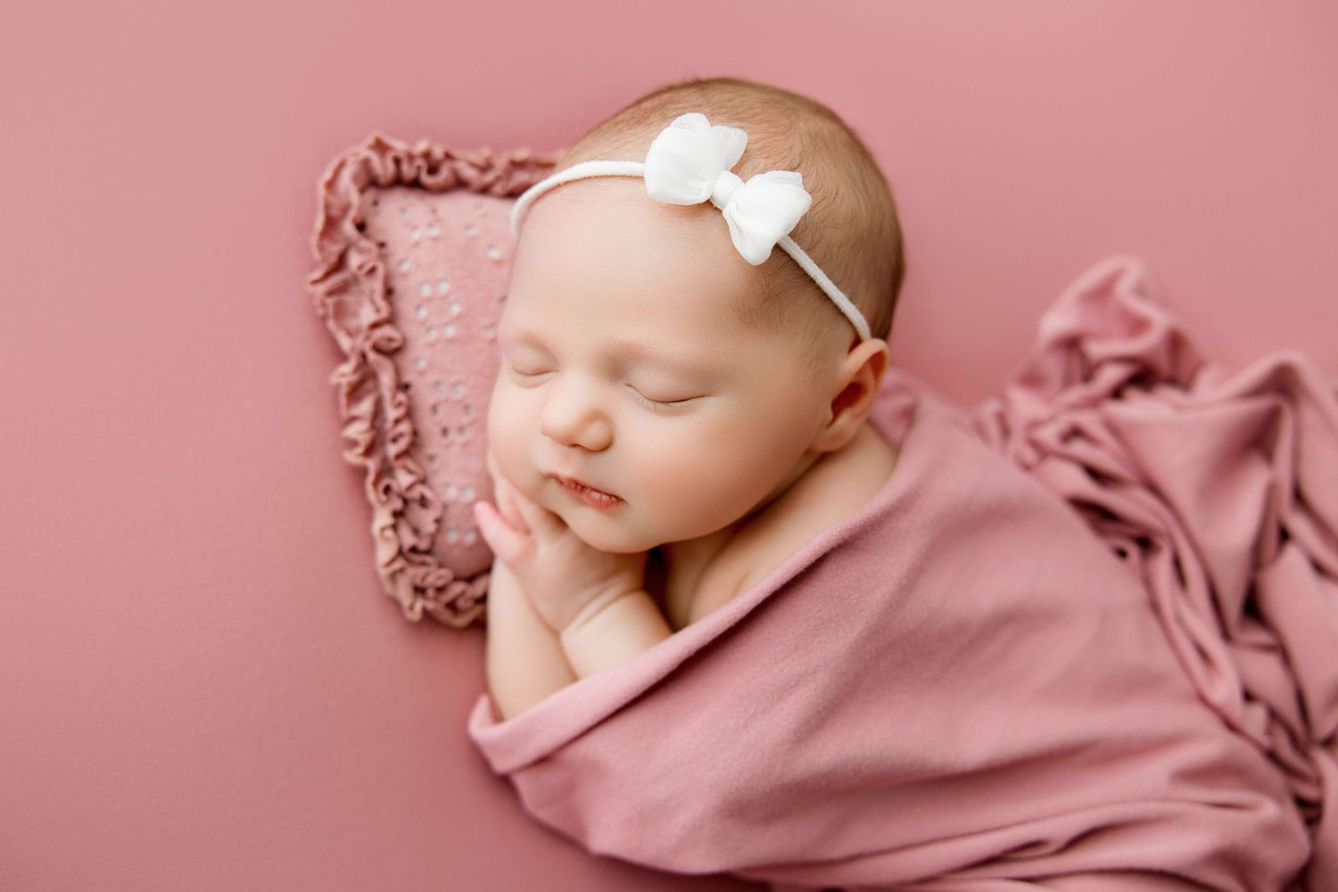 Newborn baby girl covered by pink blanket and sleeping on a pink pillow.