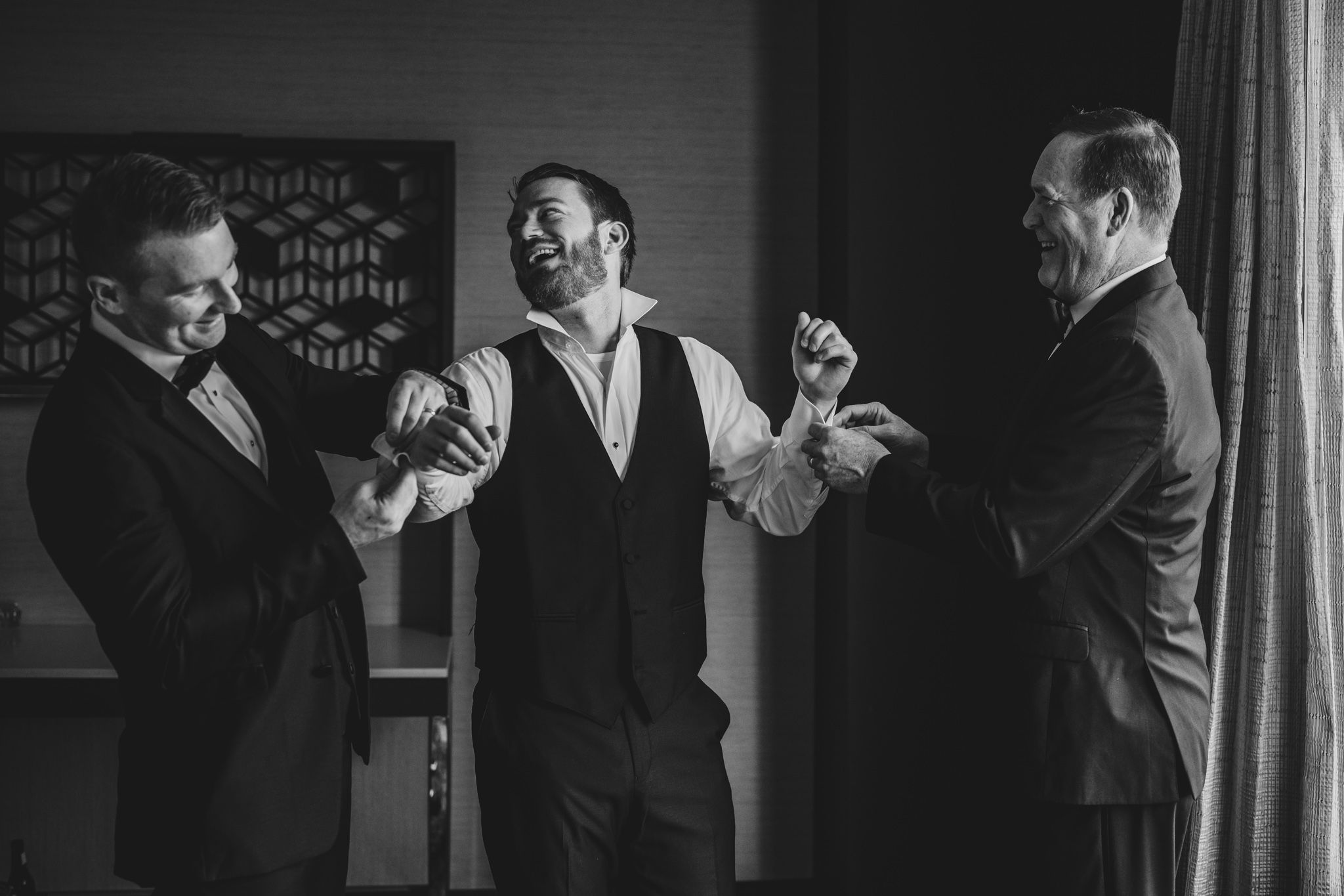 Black and white photo of three people sharing laughter in formal attire.