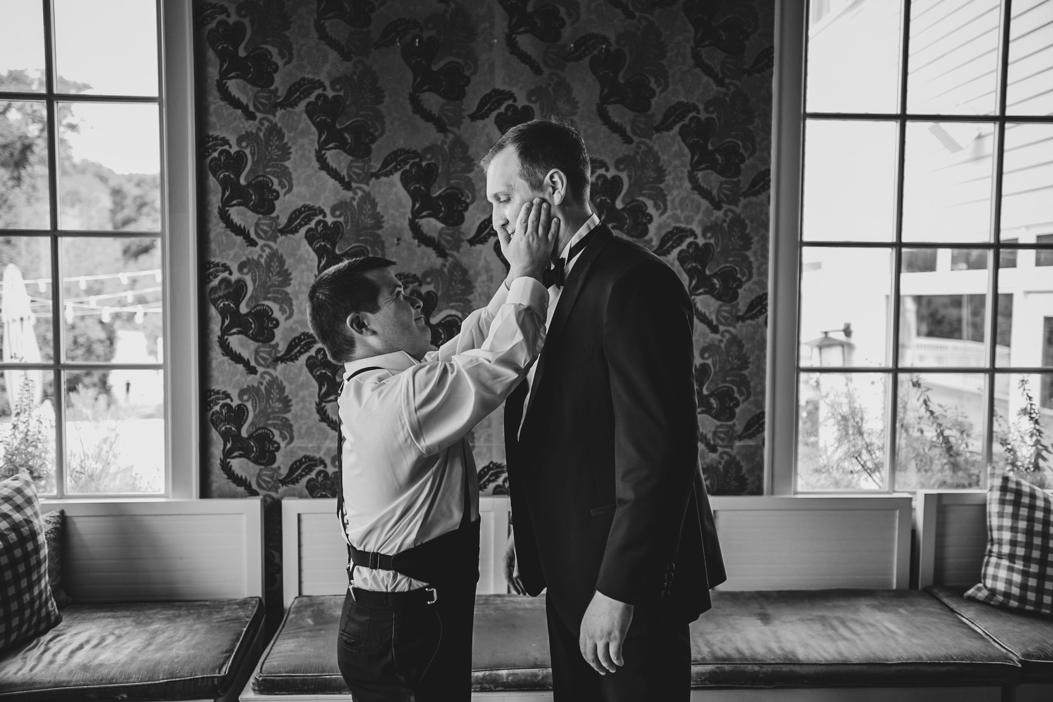 Black and white emotional moment captured by window with patterned wallpaper.