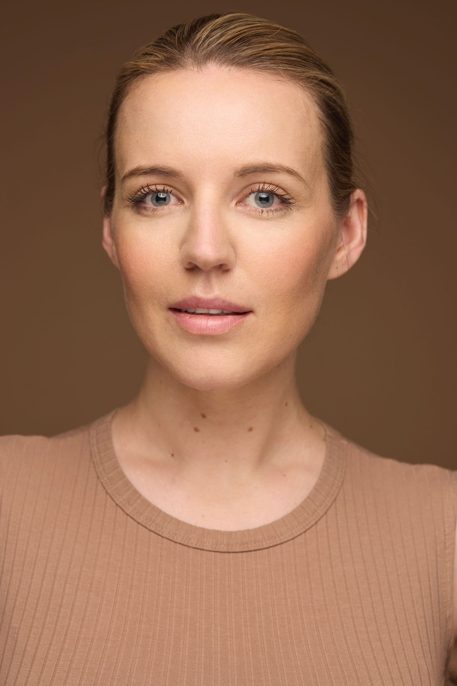 Clean beauty portrait against warm brown background wearing beige ribbed top.