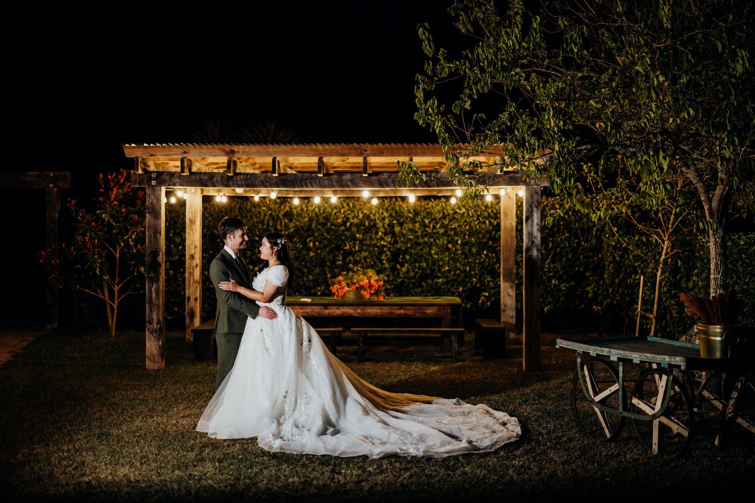 White chairs and a decorative arch are arranged for an outdoor wedding ceremony in a lush garden setting.
